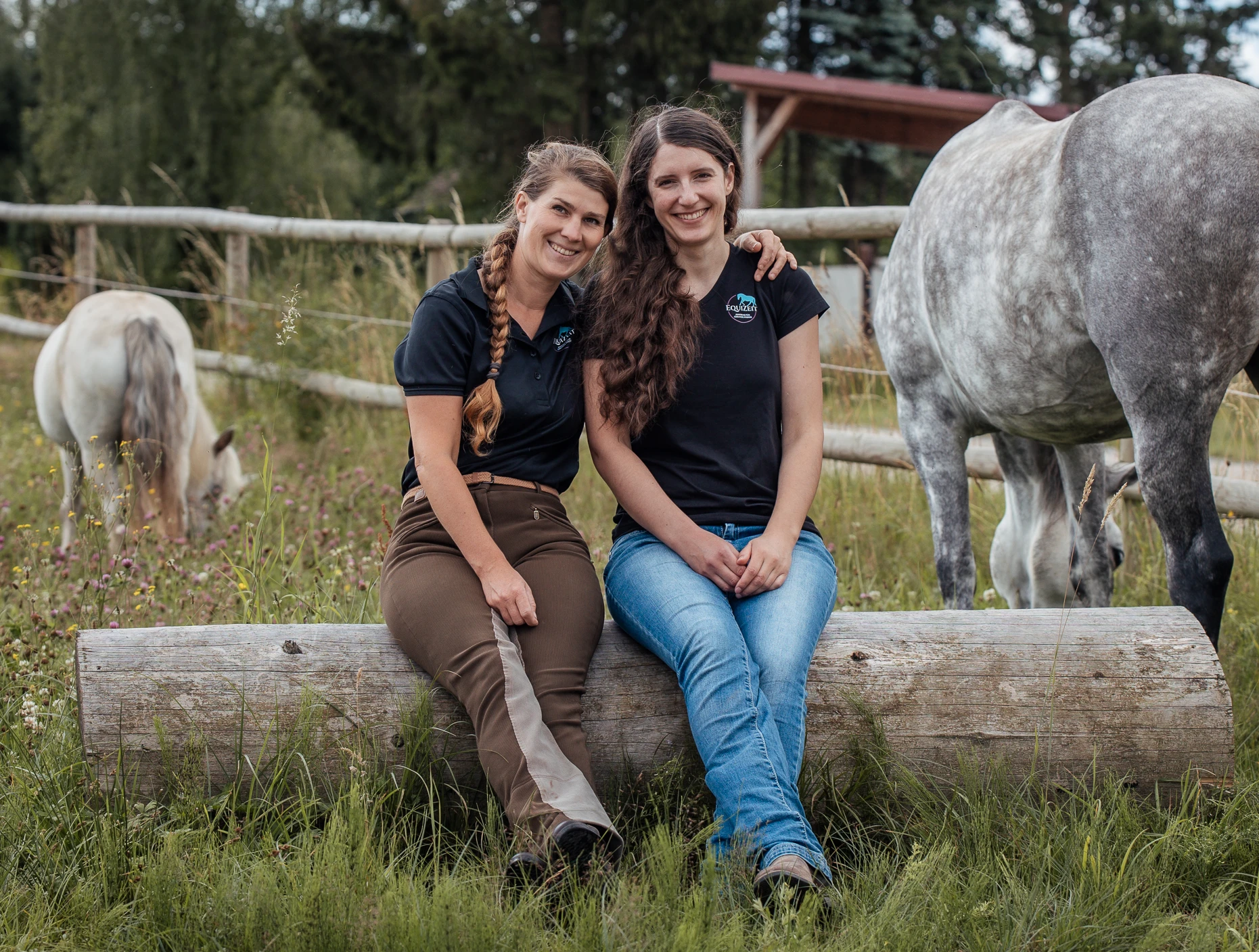 Jenny und Christine sitzen gemeinsam mit Pferden auf der Weide